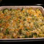 Golden-brown broccoli cheese casserole in a white baking dish with buttery cracker topping, showing creamy cheesy broccoli filling