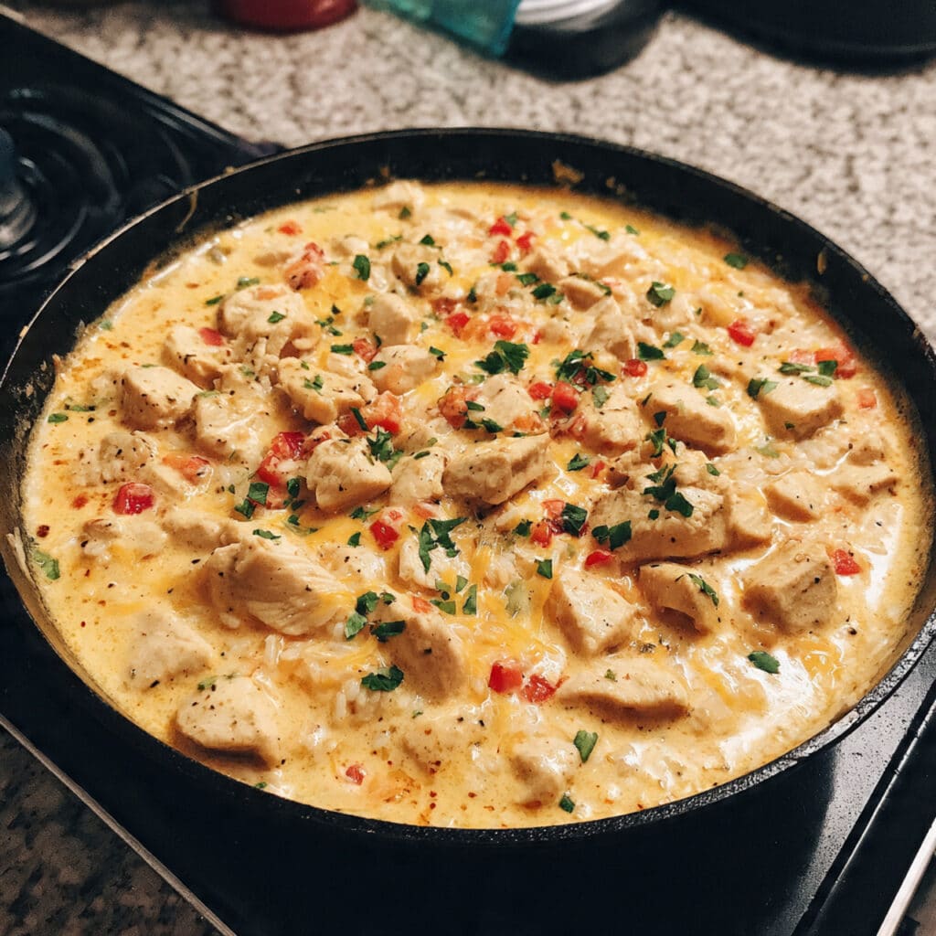 Creamy one-pot queso chicken and rice topped with melted cheese, tender chicken pieces, and colorful bell peppers.
