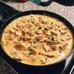Creamy one-pot queso chicken and rice topped with melted cheese, tender chicken pieces, and colorful bell peppers.
