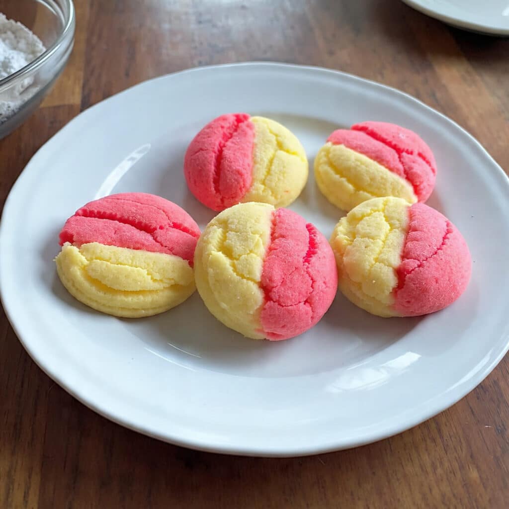 strawberry lemonade cookies with pink and yellow swirls dusted with powdered sugar on a white plate