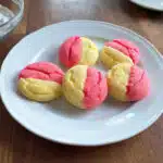 strawberry lemonade cookies with pink and yellow swirls dusted with powdered sugar on a white plate