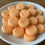 Orange cream cheese mints arranged on a white plate, showing their classic fork-pressed pattern and soft orange color