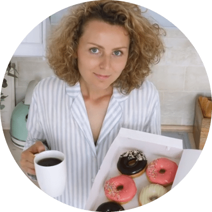 inez in a striped shirt holding a cup of coffee and a box of assorted colorful donuts in a bright kitchen.