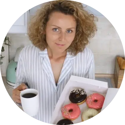 inez in a striped shirt holding a cup of coffee and a box of assorted colorful donuts in a bright kitchen.