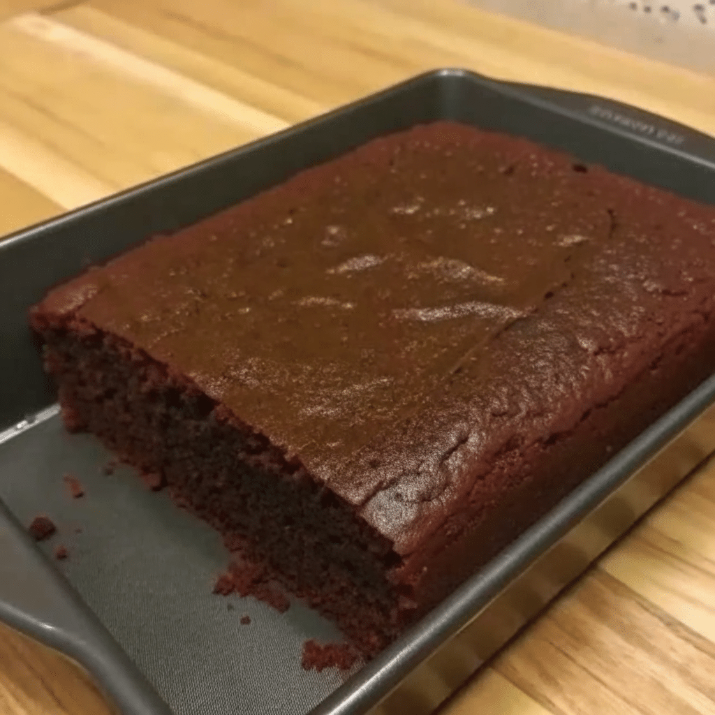 Square slice of moist gingerbread cake dusted with powdered sugar on a white plate, showing tender crumb texture with warm brown color