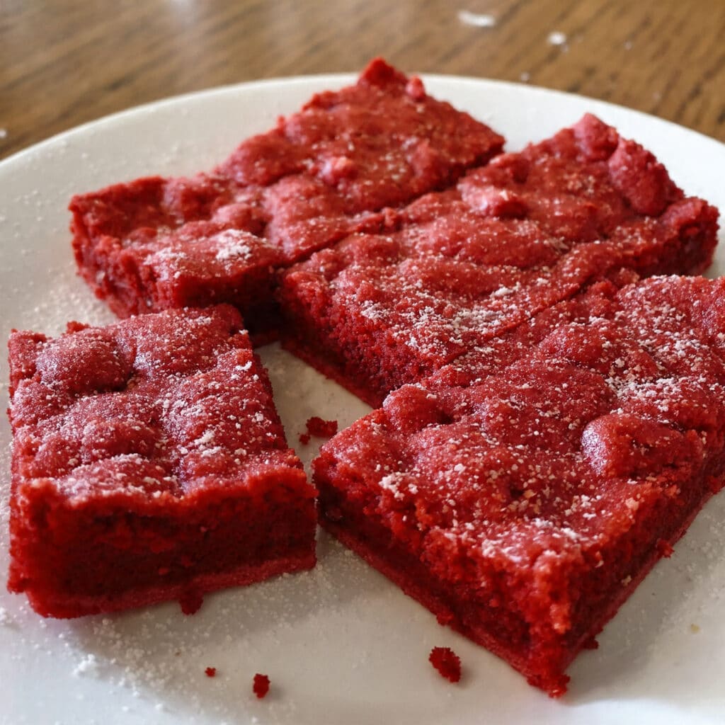 Soft and gooey red velvet cookie bars with white chocolate chips and chocolate chips, cut into squares and displayed on a white plate,