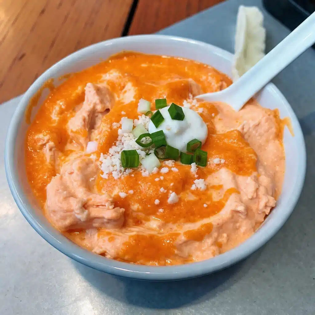 Creamy buffalo chicken dip in a small casserole dish topped with melted golden cheddar cheese and fresh green onions, served with tortilla chips and celery sticks