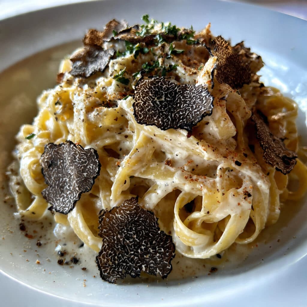 Creamy truffle pasta with Parmesan cheese served in a white bowl, garnished with black pepper and fresh herbs