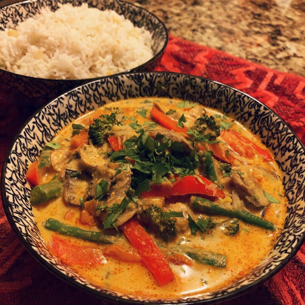 Overhead view of a vibrant Thai red curry bowl with green beans, red peppers, tofu, and basil in creamy coconut broth, served with jasmine rice.