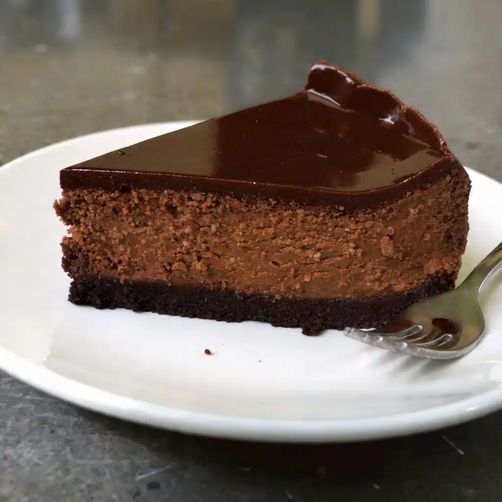 A slice of no bake chocolate cheesecake on a white plate with an Oreo cookie crust, rich chocolate mousse filling, and topped with whipped cream and chocolate shavings