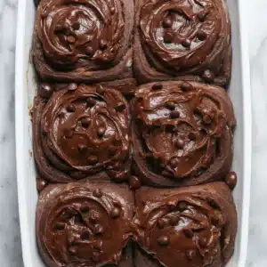 chocolate cinnamon rolls arranged in a baking dish, topped with glossy chocolate cream cheese glaze, with visible chocolate swirls throughout the soft dough