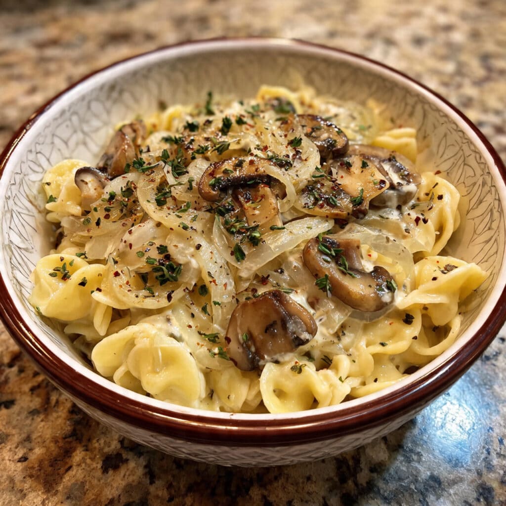 A bowl of one pot French onion pasta with caramelized onions, mushrooms, and orecchiette pasta in a rich savory sauce, garnished with fresh thyme and toasted breadcrumbs