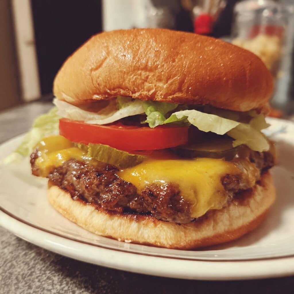 Juicy air fryer hamburgers with melted cheese on a toasted bun, topped with lettuce, tomato, pickles, and onion