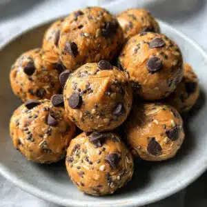 Peanut butter protein balls arranged on a white plate, showing their round shape and chocolate chip specks, with a glass of milk in the background