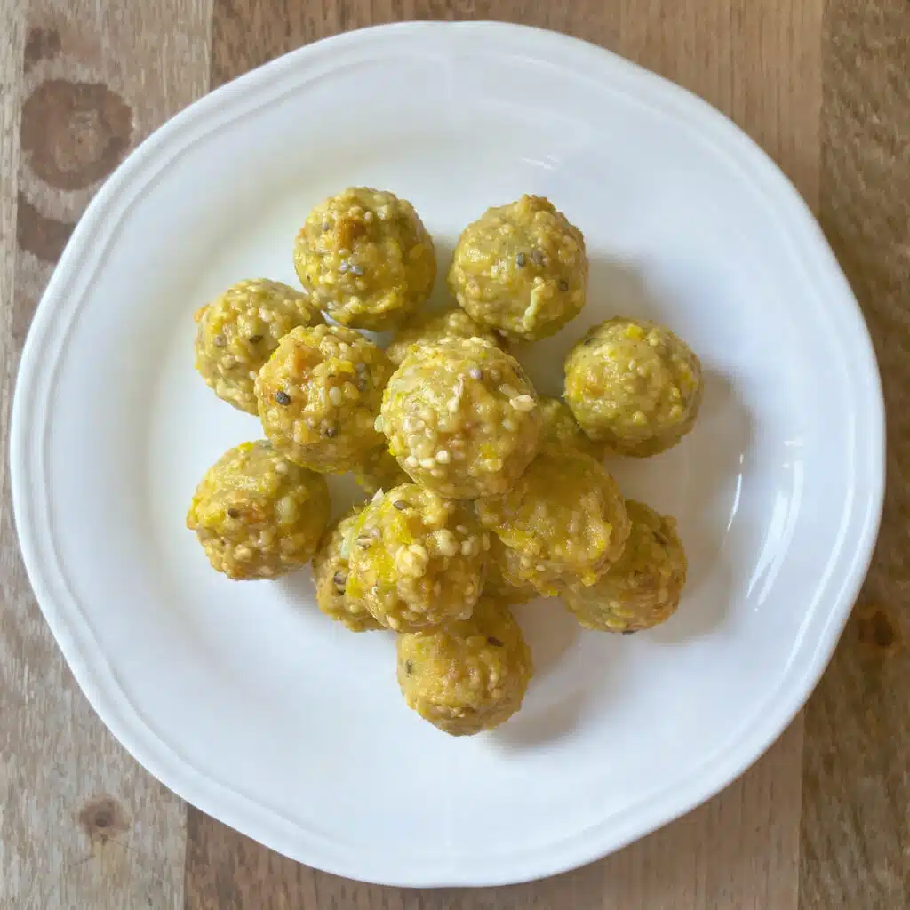 Lemon poppy seed energy bites arranged on a white plate, showing their light golden color speckled with black poppy seeds, with fresh lemon slices in the background