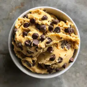Bowl of edible cookie dough loaded with chocolate chips, safe to eat raw, with a spoon scooping out a portion