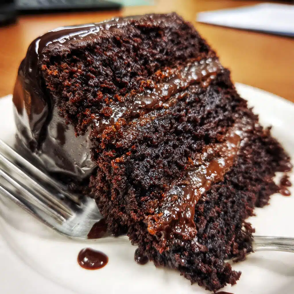 Three-layer chocolate fudge cake with rich dark chocolate frosting on a white cake stand, showing moist cake layers and smooth glossy icing