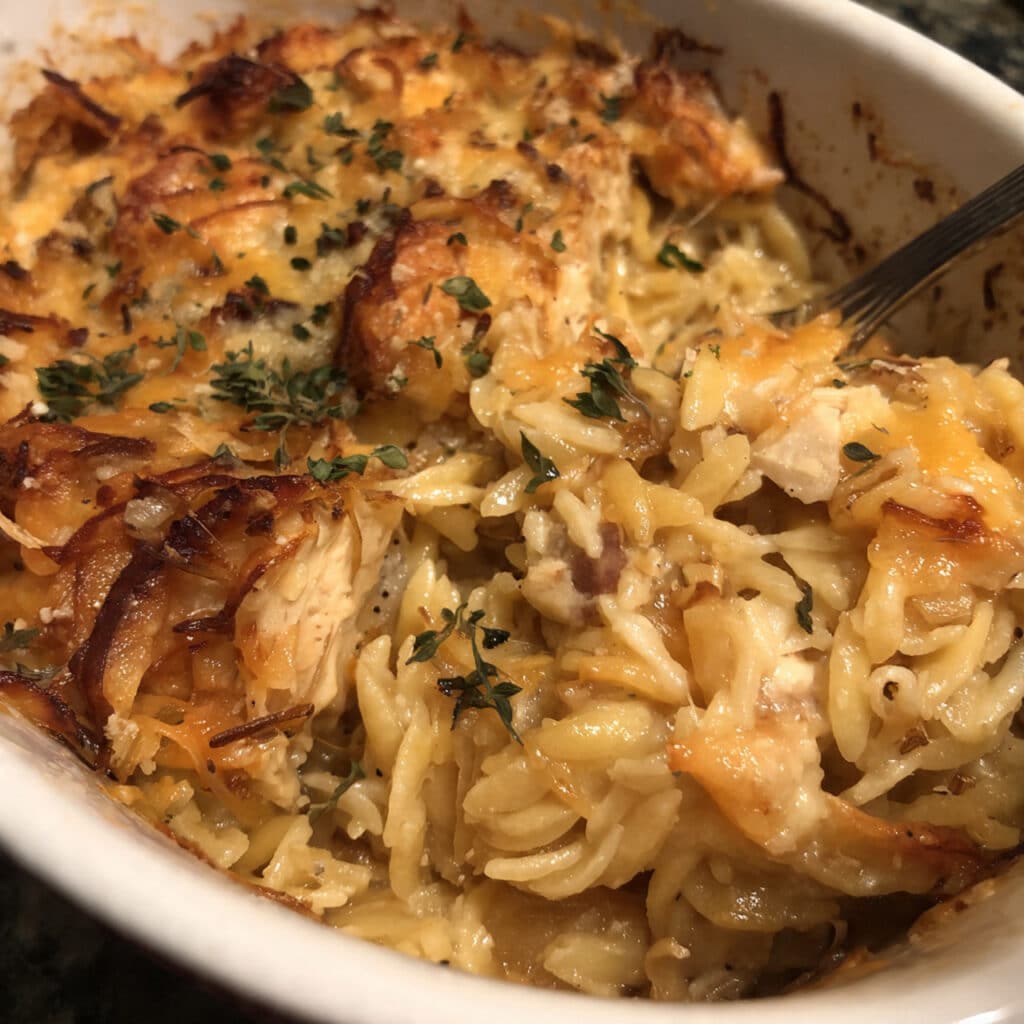 Golden bubbling French Onion Chicken Orzo Casserole in a cast iron skillet, topped with melted cheese and fresh herbs, ready to serve