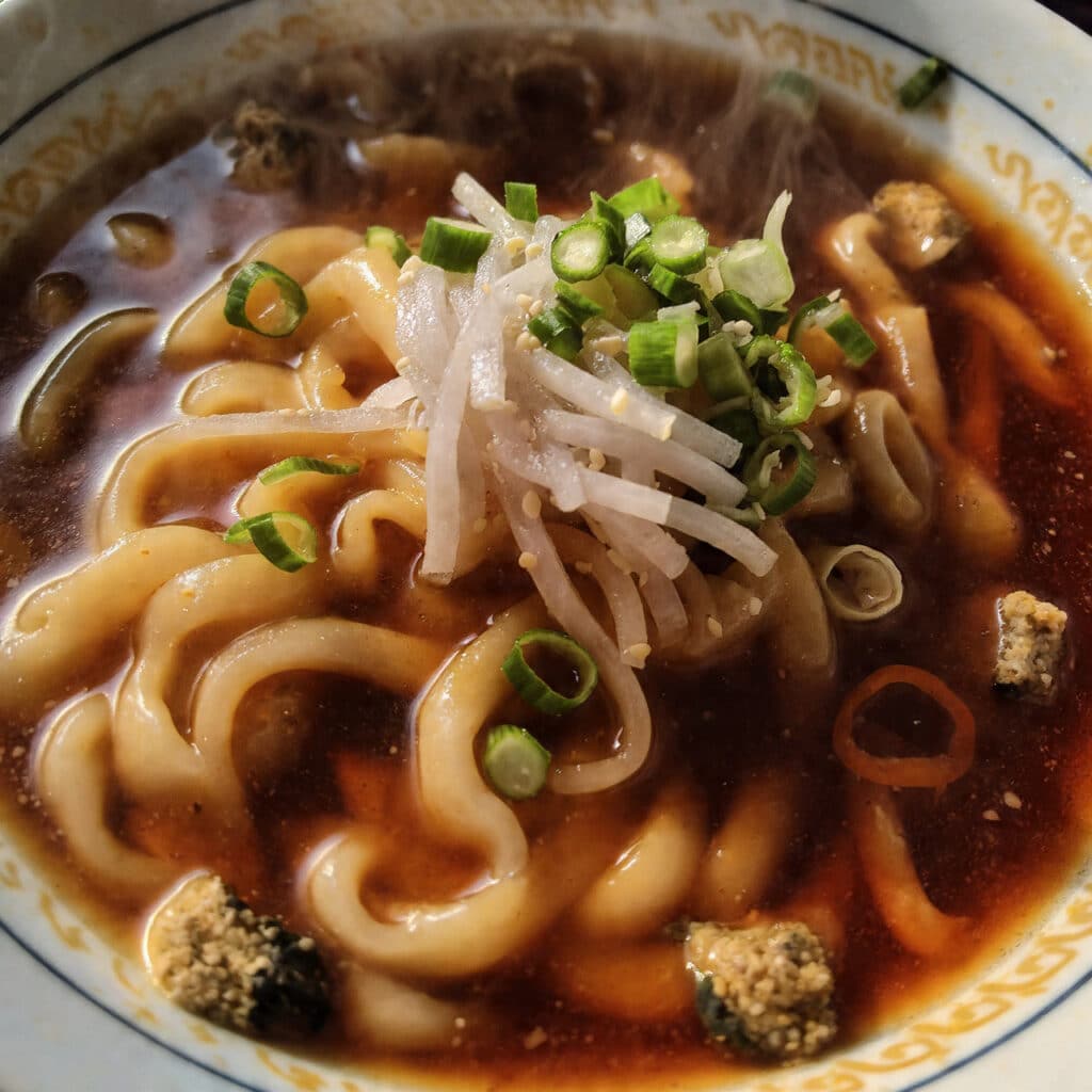 Bowl of homemade ramen noodles in savory broth topped with sliced green onions on a dark surface