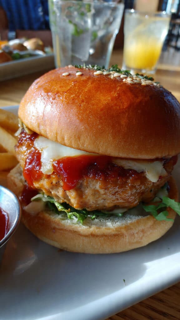 Golden-brown ground turkey burger patty on a toasted bun topped with fresh lettuce, tomato slices, red onion, and avocado on a white plate