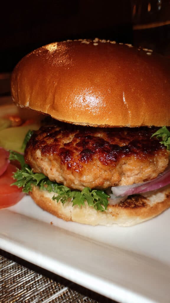 Golden-brown ground turkey burger patty on a toasted bun topped with fresh lettuce, tomato slices, red onion, and avocado on a white plate