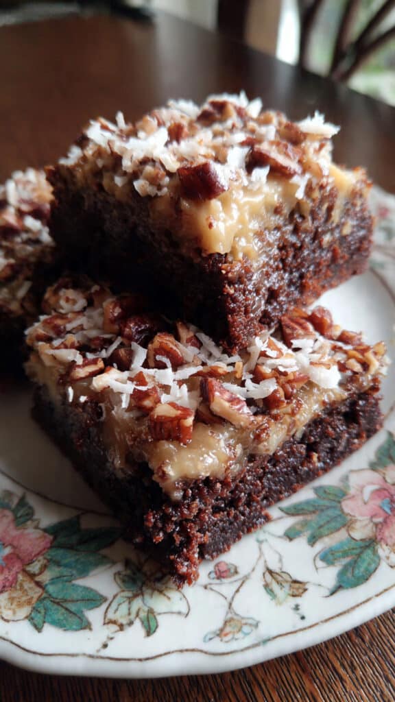 German chocolate brownies with coconut pecan topping on a white plate, showing fudgy chocolate layers and golden topping
