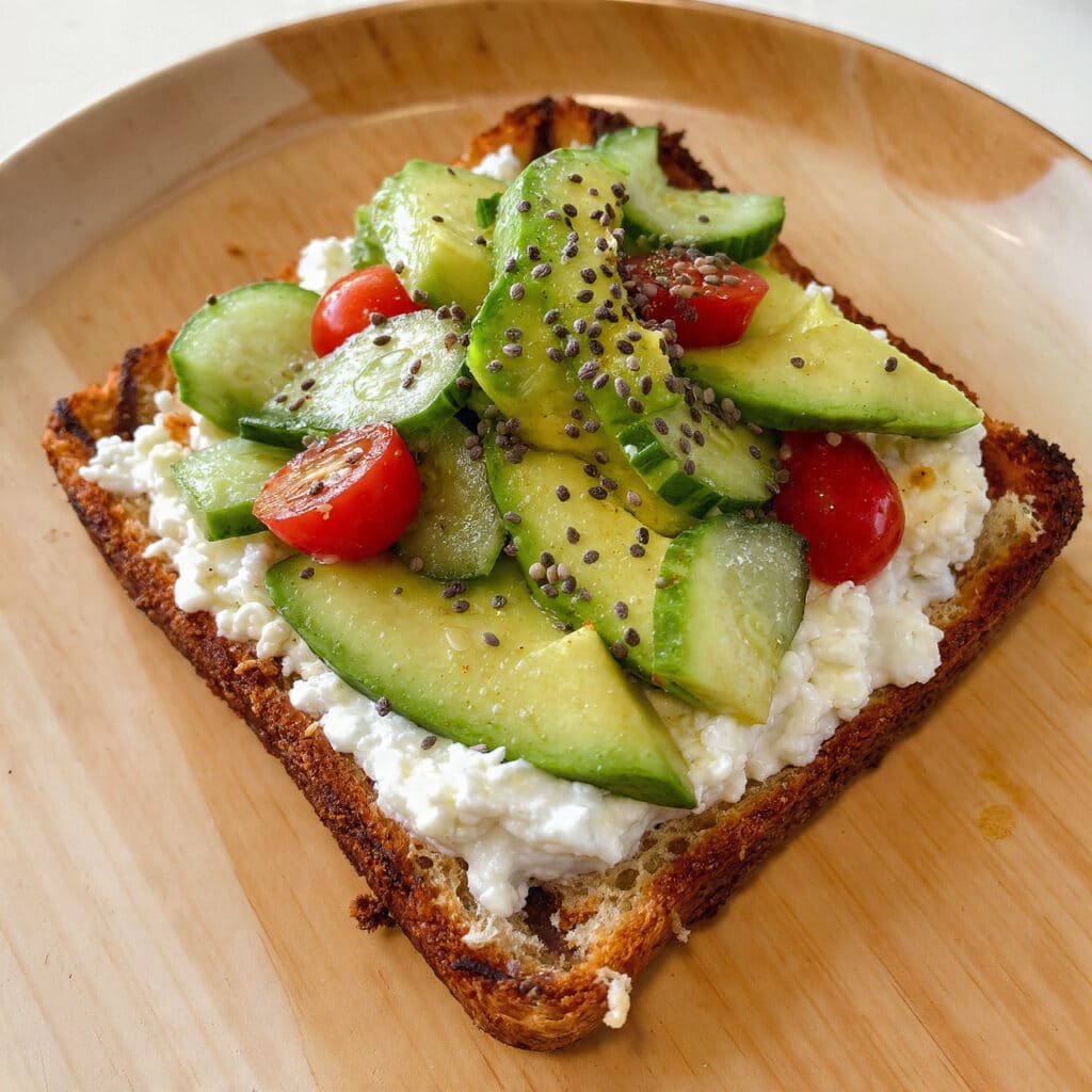 Cottage cheese toast topped with creamy avocado slices, cherry tomatoes, and fresh herbs on golden toasted sourdough bread