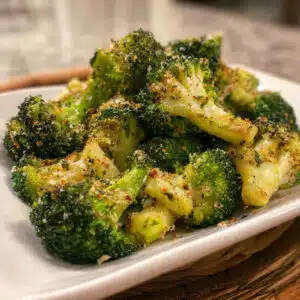 Crispy golden garlic air fryer broccoli florets on a white serving plate with optional lemon wedges and grated Parmesan cheese