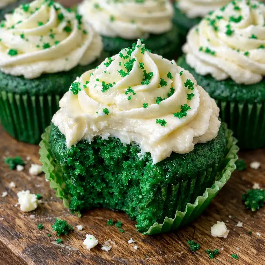 Vibrant green velvet cupcakes topped with swirls of white cream cheese frosting and festive shamrock sprinkles on a white serving plate