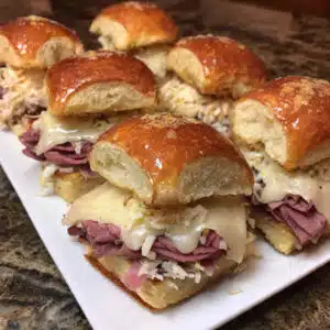 Golden-topped Reuben sliders in a baking dish with melted Swiss cheese, pastrami, and sauerkraut on soft Hawaiian rolls