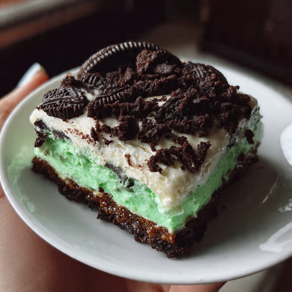 Layered Shamrock Lasagna dessert with chocolate Oreo crust, white cream cheese middle layer, and bright green mint pudding top layer