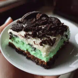 Layered Shamrock Lasagna dessert with chocolate Oreo crust, white cream cheese middle layer, and bright green mint pudding top layer