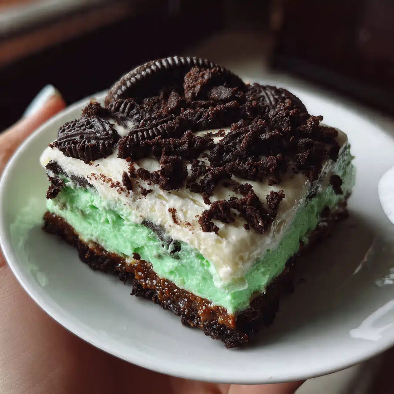 Layered Shamrock Lasagna dessert with chocolate Oreo crust, white cream cheese middle layer, and bright green mint pudding top layer