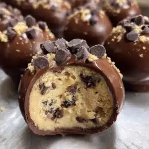 Chocolate chip cookie dough brownie bombs on a white plate with one cut in half showing the cookie dough filling inside