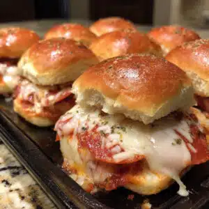 Golden brown pepperoni pizza sliders on a white plate with melted mozzarella cheese visible between soft slider buns, garnished with Italian herbs