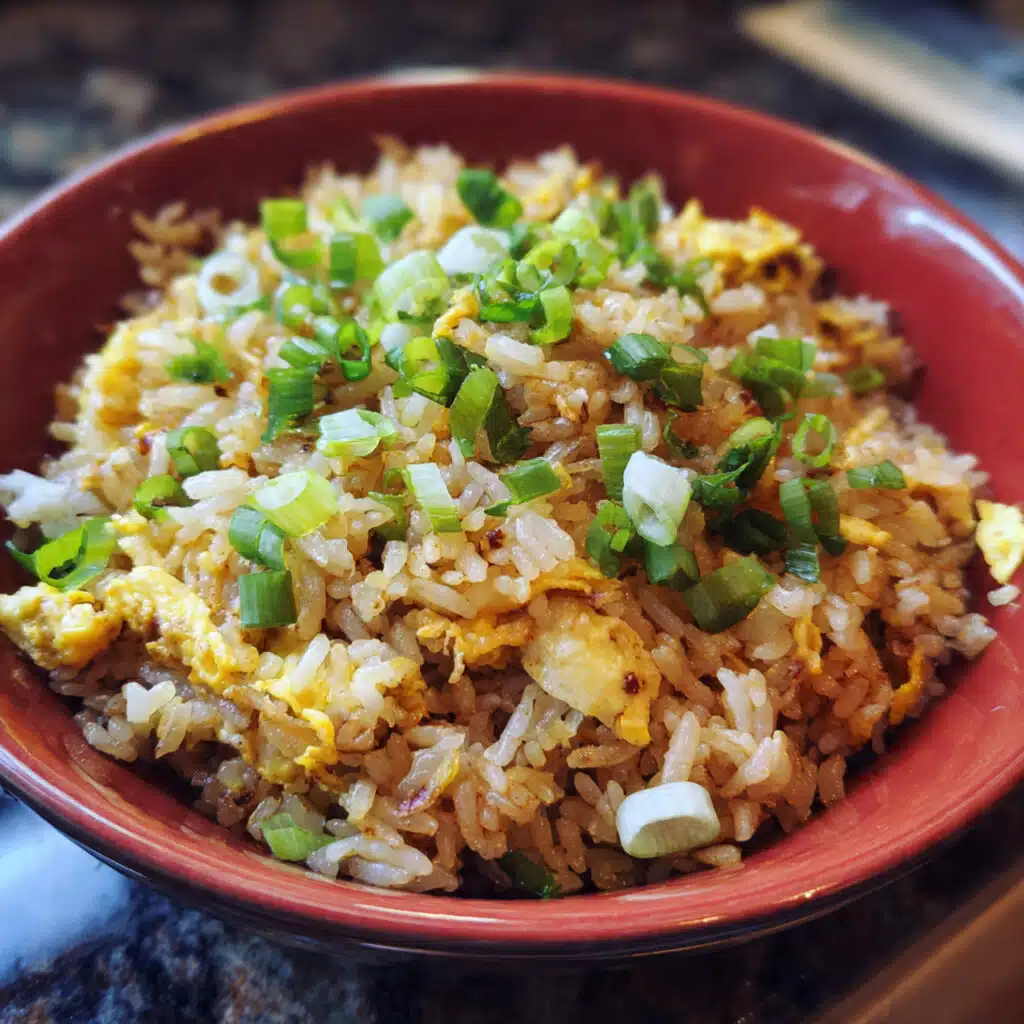 A bowl of golden egg fried rice with scrambled eggs, green onions, and chopsticks on a white plate