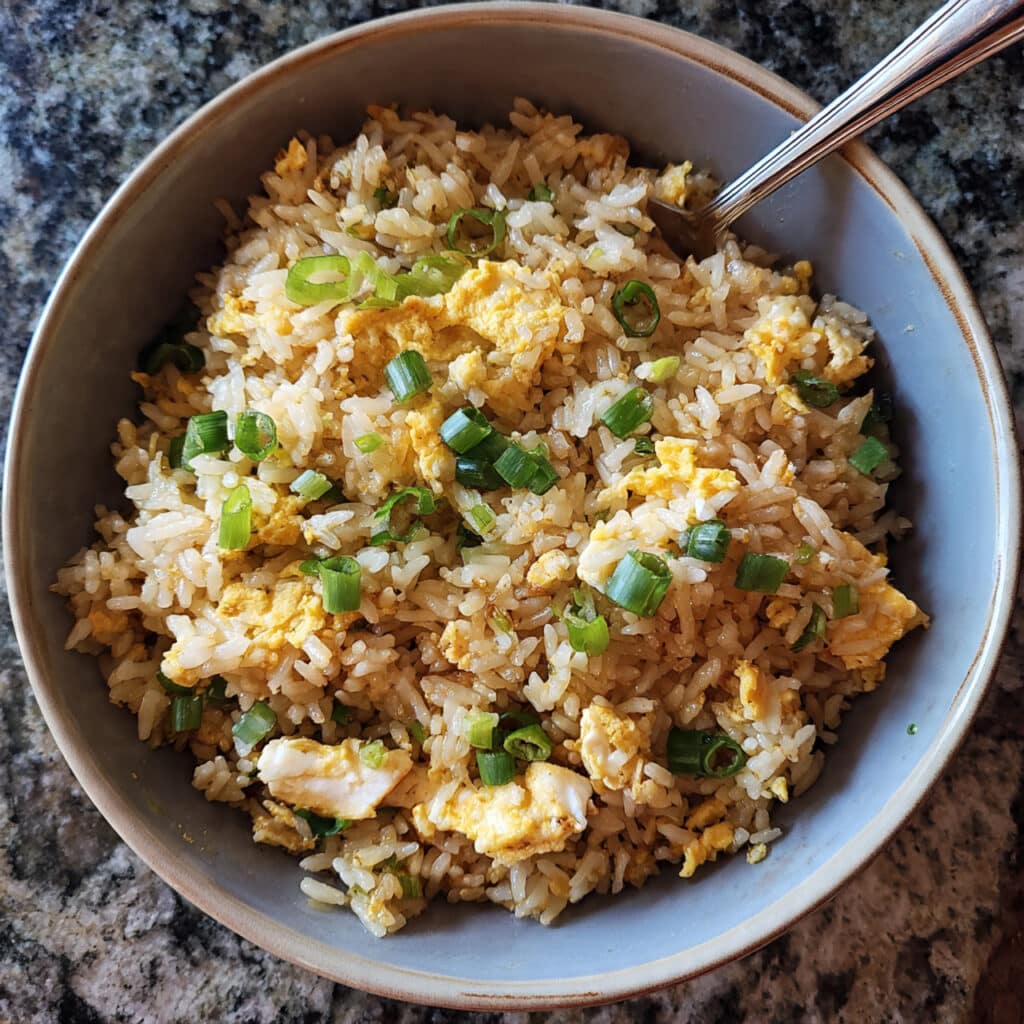 A bowl of golden egg fried rice with scrambled eggs, green onions, and chopsticks on a white plate