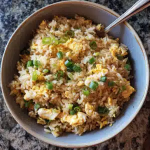 A bowl of golden egg fried rice with scrambled eggs, green onions, and chopsticks on a white plate