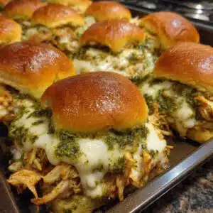 Cheesy Garlic Pesto Chicken Sliders 9 Golden-brown cheesy garlic pesto chicken sliders in a baking dish, showing melted mozzarella and herb-topped slider buns