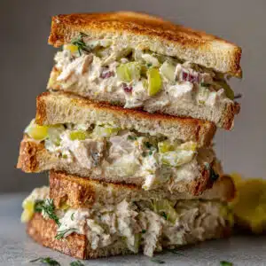 Tuna Salad Sandwich 8 Creamy tuna salad sandwich on toasted wheat bread with crisp lettuce and fresh tomato slices, served with pickle spears and chips on a white plate