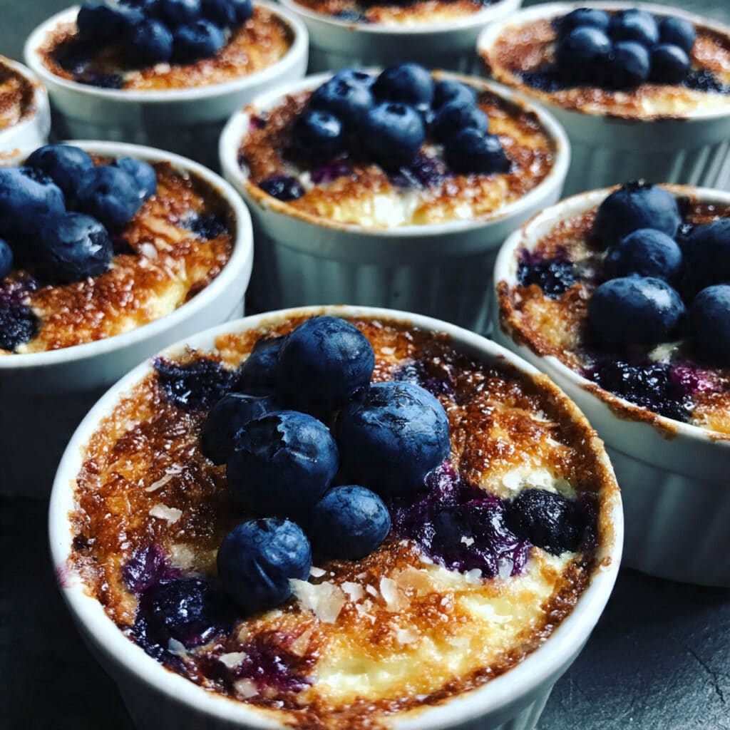 Golden-baked blueberry cottage cheese bowls in white ramekins topped with fresh blueberries, sliced almonds, and a drizzle of honey on a rustic wooden table