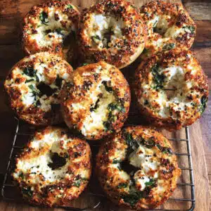 Golden-brown cottage cheese flagels topped with everything bagel seasoning on a white plate, showing soft, tender texture with visible spinach flecks