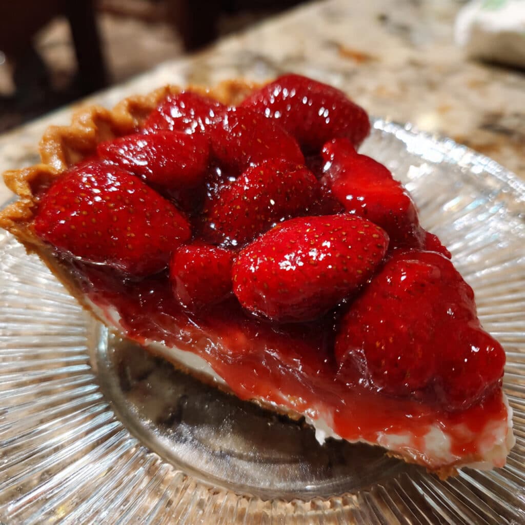 Strawberry Pie 2 strawberry pie with glazed red strawberries in a golden pie crust, topped with whipped cream on a white plate