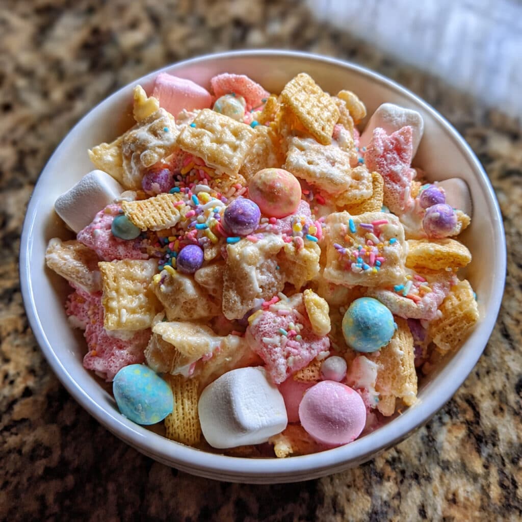 Easter Bunny Chow snack mix with white chocolate coated cereal, mini marshmallows, and candy in a clear glass bowl
