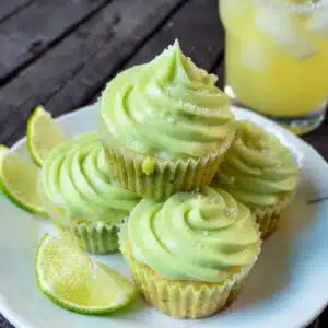 Margarita cupcakes topped with tequila lime buttercream frosting, garnished with fresh lime slices and coarse sugar on white serving platter