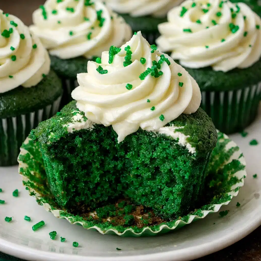 Vibrant green velvet cupcakes topped with swirls of white cream cheese frosting and festive shamrock sprinkles on a white serving plate