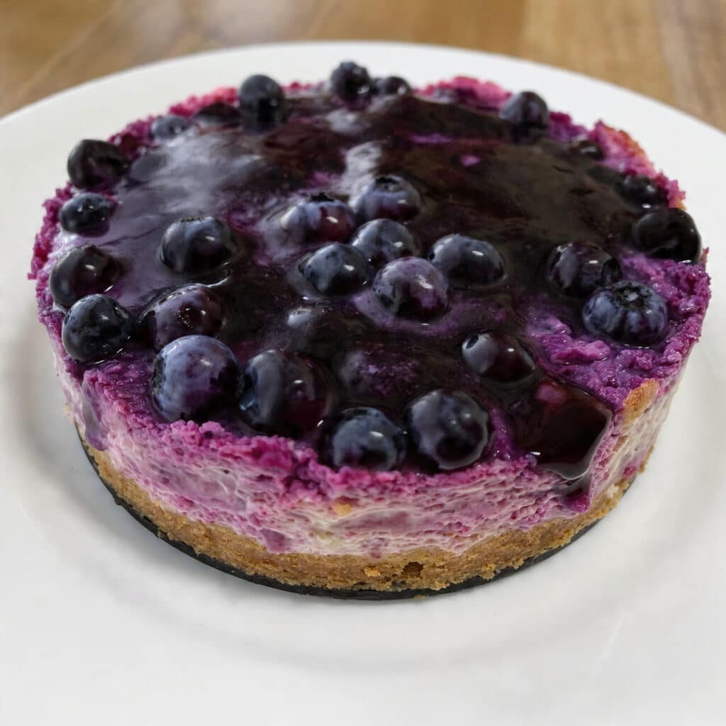 Smooth, vibrant purple blueberry curd in a glass jar with fresh blueberries scattered nearby