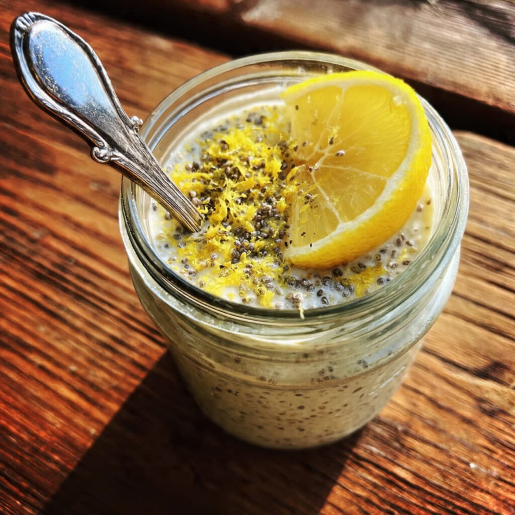 lemon chia pudding in a clear glass bowl topped with fresh berries and lemon zest showing the thick pudding texture