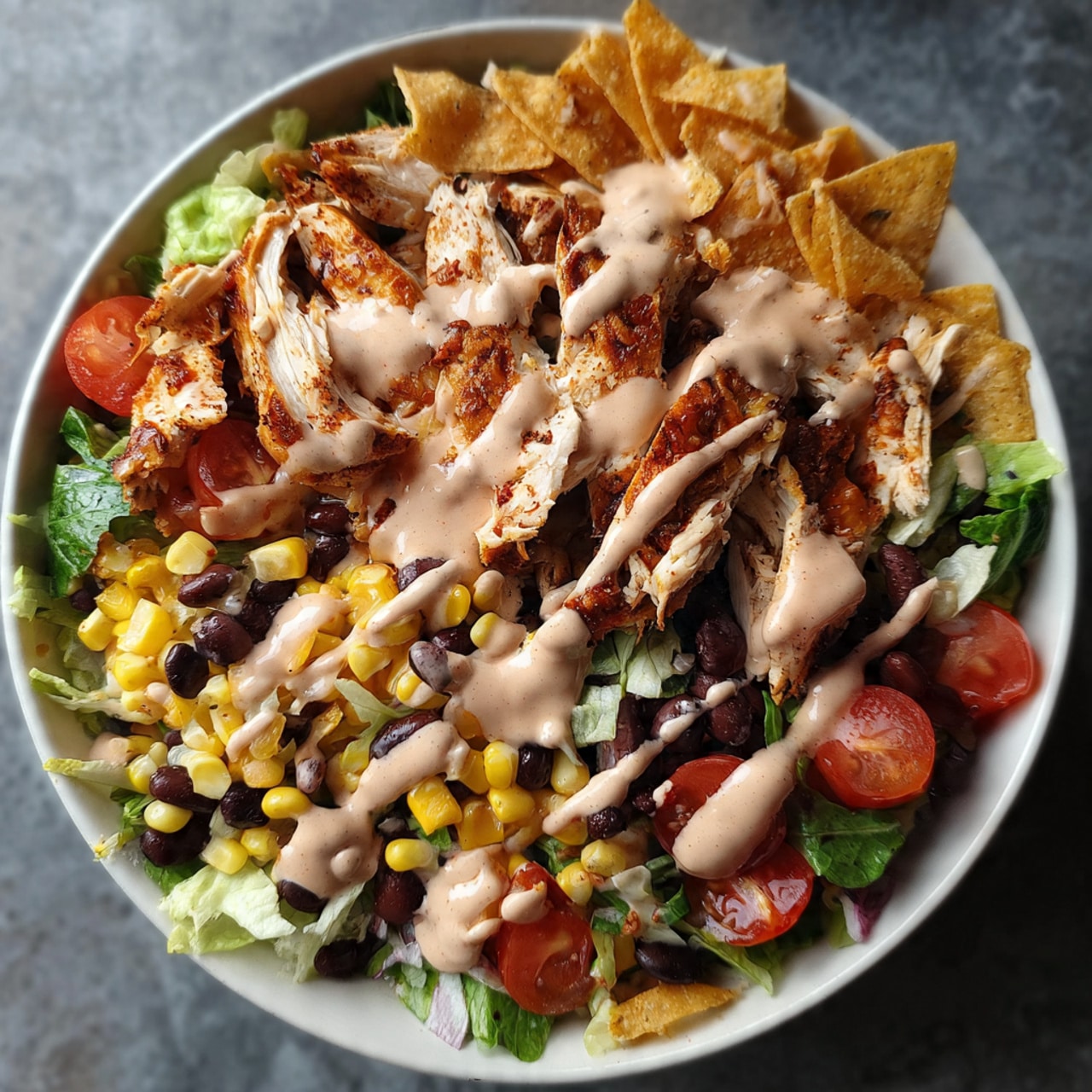 BBQ chicken salad on a white plate loaded with grilled chicken, black beans, corn, tomatoes, red onion, and tortilla chips with BBQ ranch dressing
