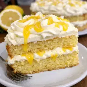 A slice of limoncello mascarpone cake on a white plate, showing moist yellow cake topped with fluffy white mascarpone frosting swirled with golden lemon curd